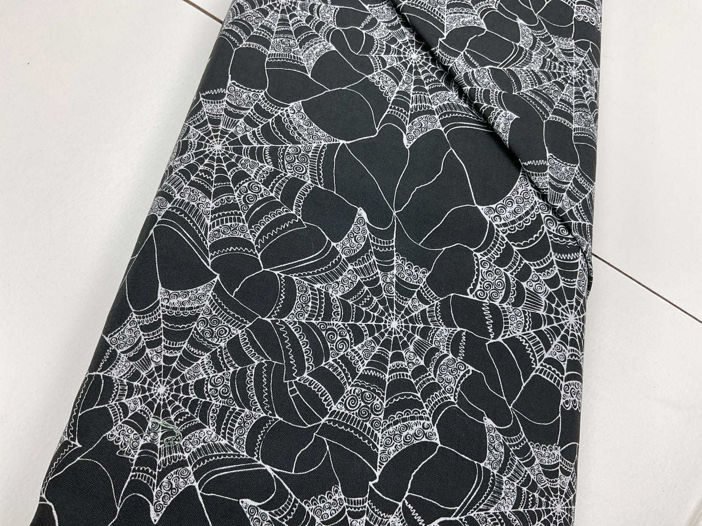 Black fabric with white spider web pattern with swirl details on the web