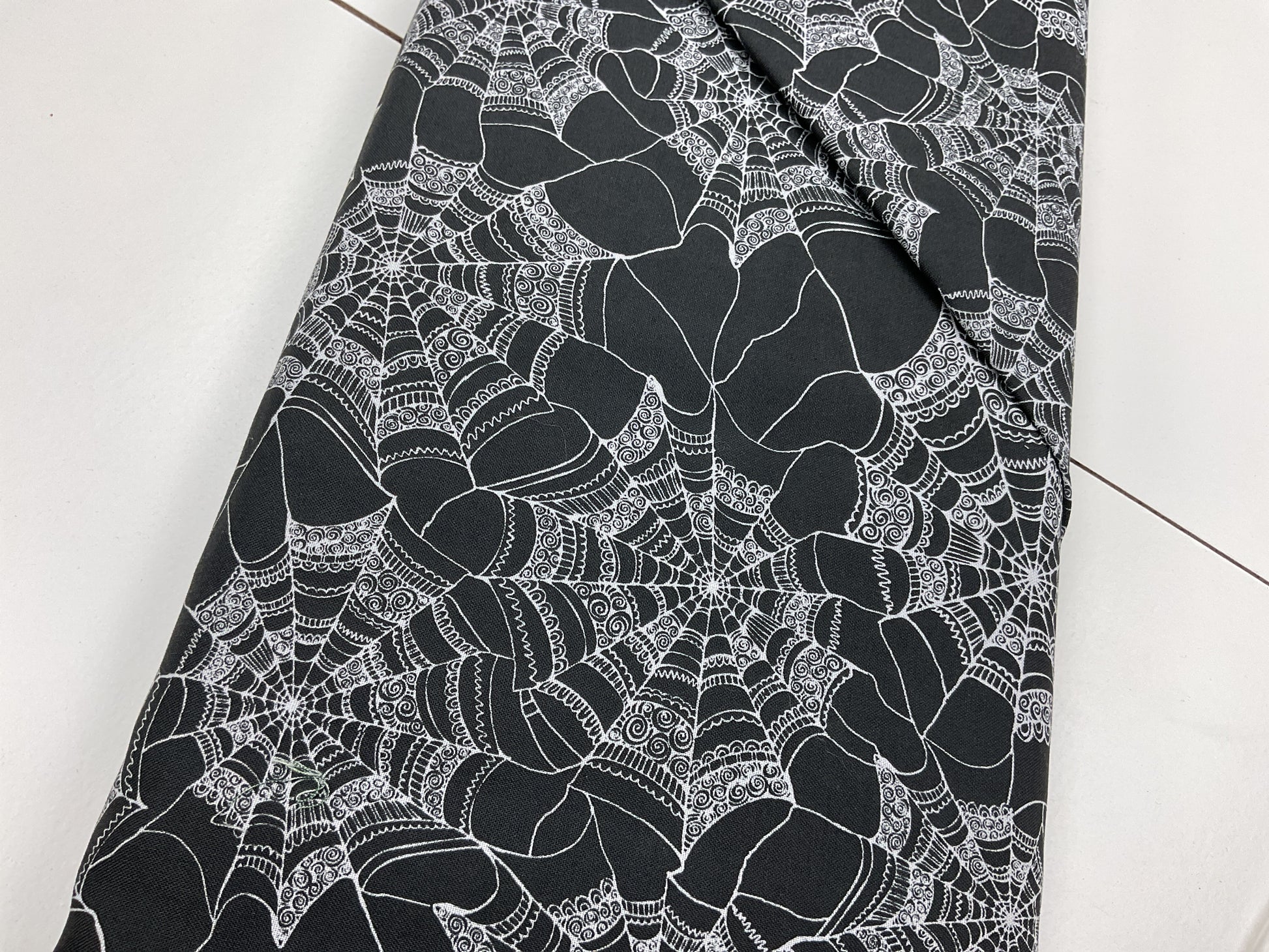 Black fabric with white spider web pattern with swirl details on the web